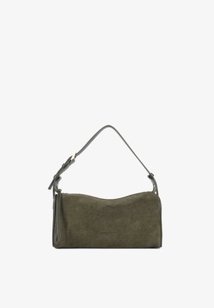 Sac à main en daim vert olive avec une courte bandoulière en cuir réglable et un petit pompon latéral, présenté sur fond blanc.