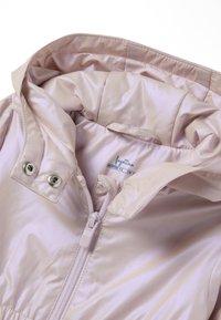 Giacca di tessuto satinato rosa pallido con cappuccio, dotata di chiusura frontale con zip, bottoni a pressione e una morbida fodera interna. Etichetta del brand visibile all'interno.