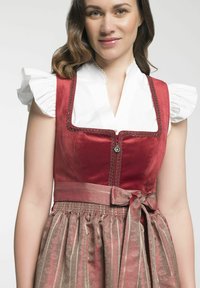 Rode fluwelen lijfje met kanten afwerking, witte gerimpelde mouwen en een goudgestreepte rok. Inclusief een tailleband en een decoratieve knoop.
