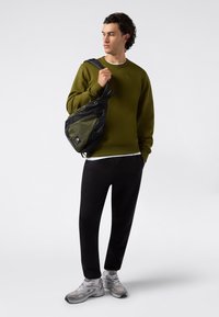 Oliwkowy sweter, czarne spodnie i szare sneakersy. Torba ma mieszankę czarnego i zielonego materiału z zamkami błyskawicznymi i paskiem na ramię.