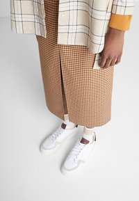 Brun rutig midilång kjol med slits fram, ihopparad med vita sneakers och randiga strumpor. En beige rutig skjorta kompletterar outfiten.