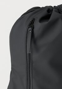 Μαύρο σακίδιο κατασκευασμένο από υλικό με υφή, με κλείσιμο φερμουάρ και κορδόνι στο πάνω μέρος, με κομψό και μοντέρνο σχεδιασμό.