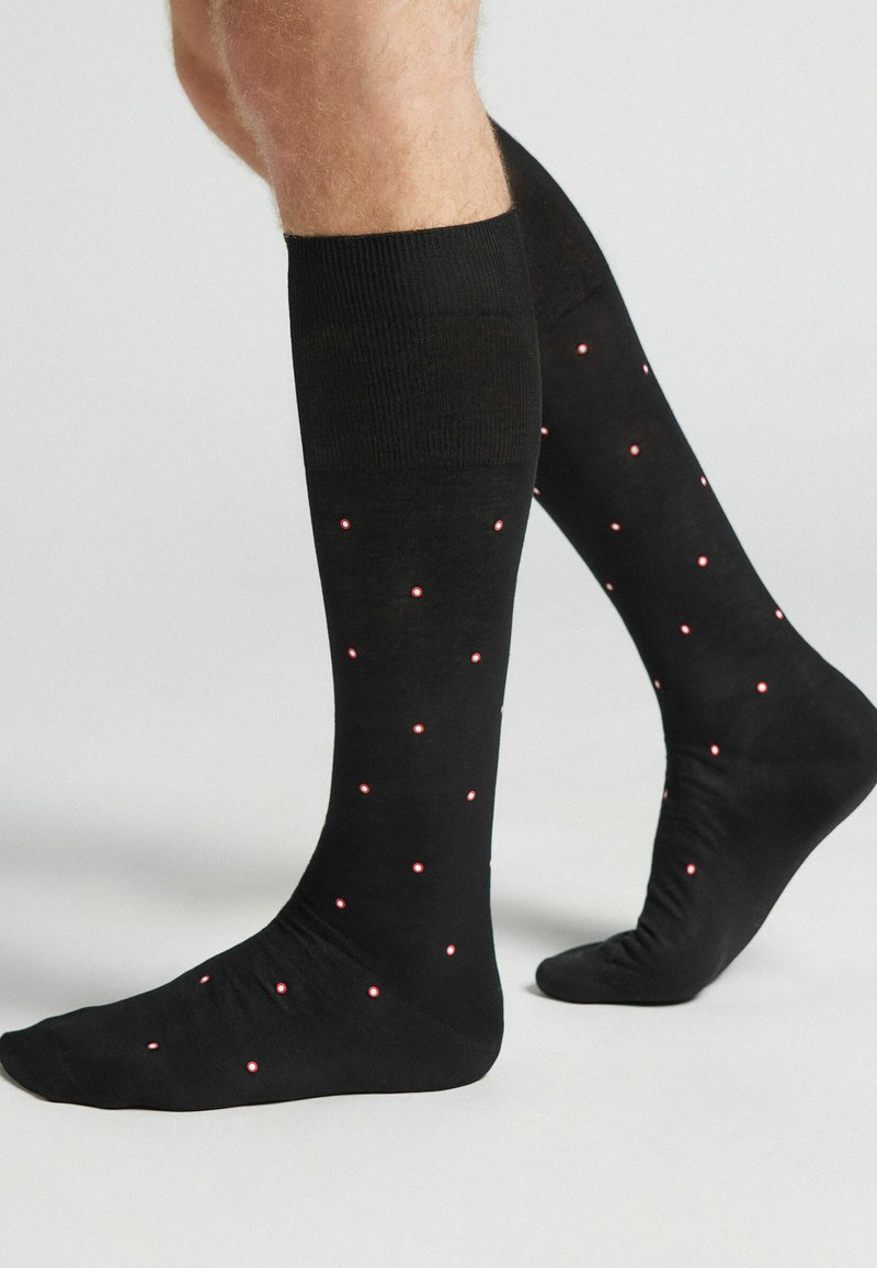 Medias altas negras hasta la rodilla con un patrón de pequeños puntos rojos. Fabricadas con un material suave y elástico, con un borde acanalado en la parte superior.