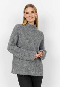 Grå stickad tröja med hög krage, ribbstruktur och lösa ärmar. Har en avslappnad passform och en fransig nederkant för extra detalj.