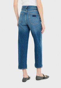 Jeans de mezclilla azul de talle alto, con un corte relajado, que cuentan con dos bolsillos traseros y puños con dobladillo. La textura es suave con un acabado clásico de mezclilla.