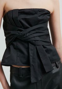 Černý top bez ramínek se strukturovaným designem, s překrouceným detailem vpředu a splývavými kravatami v pase, vyrobený z hladké tkaniny.