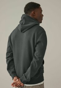 Sudadera gris oscuro con una gran capucha y puños acanalados. Tejido suave con un corte relajado, que presenta una parte posterior lisa sin patrones ni acentos visibles.