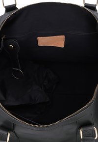Schwarzer Lederhandtaschen-Innenraum mit Reißverschlusstasche, kleinem Schlüsselband und eingenähtem hellbraunem Etikett innen.