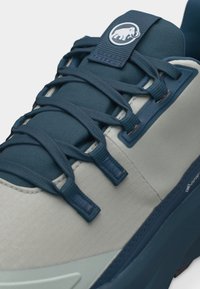 Μπλε και γκρι παπούτσι πεζοπορίας με σκούρα μπλε κορδόνια, επενδυμένη γλώσσα με λευκό λογότυπο μαμούθ και ετικέτα Gore-Tex στο πλάι.