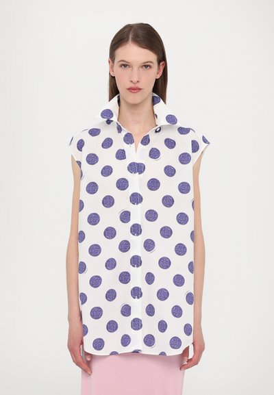 Chemise blanche à pois bleus, à manches courtes et avec un col haut et replié. Présente un devant à boutons et un design ample et décontracté.