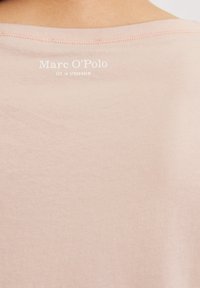 Lichtroze katoen t-shirt met een ronde hals en een ontspannen pasvorm. Heeft witte logotekst op de achterkant nabij de halslijn. Soepele textuur.