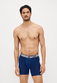 Marineblå boxer briefs med en grå Nike-logo på taljen, lavet af et blødt, strækbart materiale. Har et tætsiddende design og længde til midt på låret.