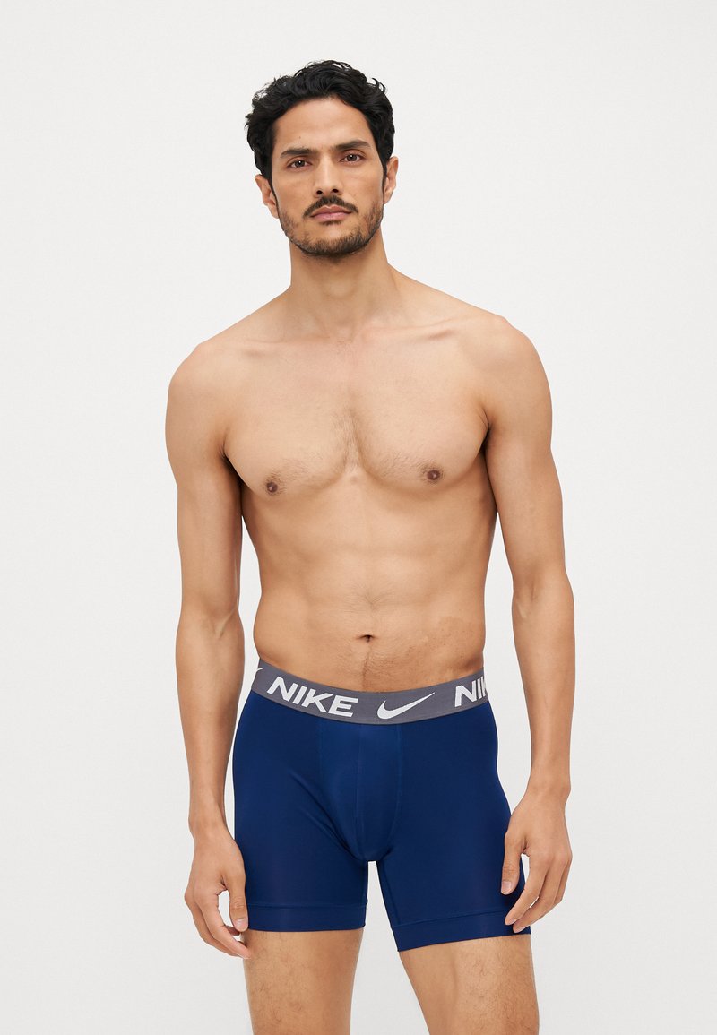 Marineblå boxer briefs med en grå Nike-logo på taljen, lavet af et blødt, strækbart materiale. Har et tætsiddende design og længde til midt på låret.