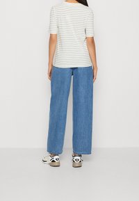 camisa de rayas de manga corta en blanco y negro, combinada con jeans de mezclilla azules holgados y zapatillas deportivas con un logo en blanco y negro.
