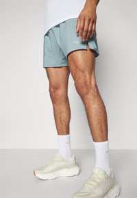 Pantalones cortos deportivos de color azul claro con cortes laterales y un pequeño logo. Combinados con zapatillas de correr beige y calcetines blancos. Tela suave y transpirable.
