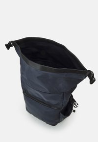 Zaino roll-top blu navy realizzato in tessuto resistente. Presenta una tasca frontale con zip, spallacci regolabili e una fodera interna morbida.