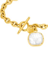 Pulsera de cadena en tono dorado con un cierre de toggle, que presenta un colgante ovalado de piedra blanca lisa grabado con un diseño y una etiqueta de marca.