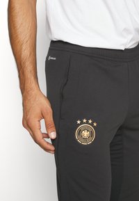 Svarta joggerbyxor med elastiskt midjeband, prydda med en gul logotyp och fyra stjärnor, tillverkade av mjukt och stretchigt tyg för komfort.