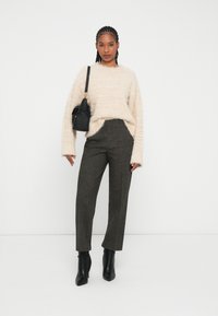 Maglione cremoso e soffice con maniche larghe, pantaloni grigi a quadri a vita alta e stivaletti neri alla caviglia. Borsa piccola nera indossata a tracolla.