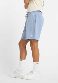 Light blue cotton shorts with an elastic waistband, drawstring, and side pockets. White logo visible on the left leg. Paired with white sneakers.