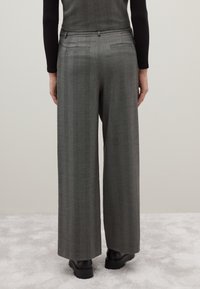 Pantaloni grigi a gamba larga con un motivo testurizzato, dotati di tasche posteriori e una vestibilità su misura. Indossati con scarpe nere su un tappeto chiaro.