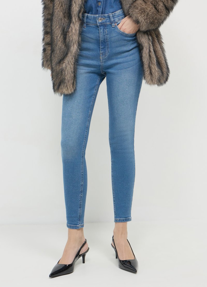Jeans bleus taille haute avec une coupe slim, en denim. Associés à des escarpins à talons slingback en cuir verni noir et à un manteau en texture fourrure.