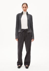 Twee-delige outfit bestaande uit een geribbelde, grijze zip-up cardigan en een witte coltrui. Gecombineerd met donkergrijze broek en zwarte instapschoenen.