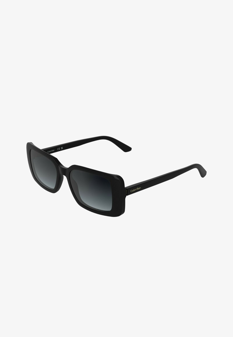 Lunettes de soleil rectangulaires Calvin Klein noires avec verres foncés dégradés et branches fines sur fond blanc.