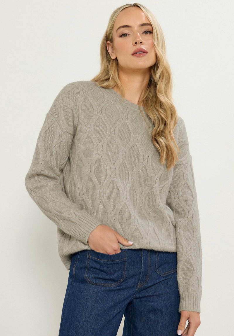 Lys grå sweater med et struktureret diamantmønster, dropped shoulders og ribbede manchetter. Parret med mørkeblå jeans.