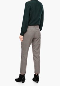 Rutiga byxor i ljusa och mörka nyanser med smal passform, i kombination med en mörkgrön blus med långa ärmar och svarta ankelskor.