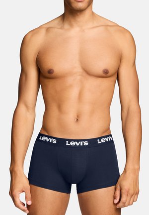 Männliches Model trägt navyblaue Levi's Boxershorts mit Markenbund, steht vor hellem, einfarbigem Hintergrund, der Oberkörper ist sichtbar.