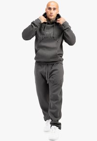 Grå hættebluse og matchende sweatpants lavet af blødt materiale, med et stort præglogo, afslappet pasform og justerbar snor i taljen.