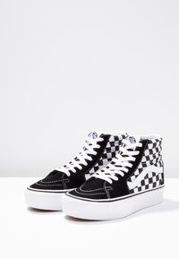 Schwarz-weiße High-Top-Sneaker mit einem Schachbrettmuster, einem Obermaterial aus Wildleder, weißen Schnürsenkeln und einer weißen Gummisohle mit Nähdetails.