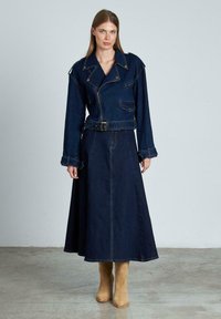 Chaqueta de mezclilla con un diseño de moto, de color azul oscuro, que presenta un cinturón, bolsillos y grandes solapas, combinada con una larga falda de mezclilla a juego.