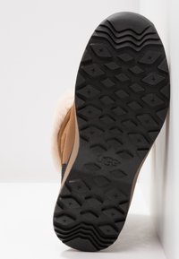 Botte en daim marron avec une doublure en peau de mouton blanche  ; semelle en caoutchouc noir texturée avec un motif de bande diagonale pour une meilleure traction.