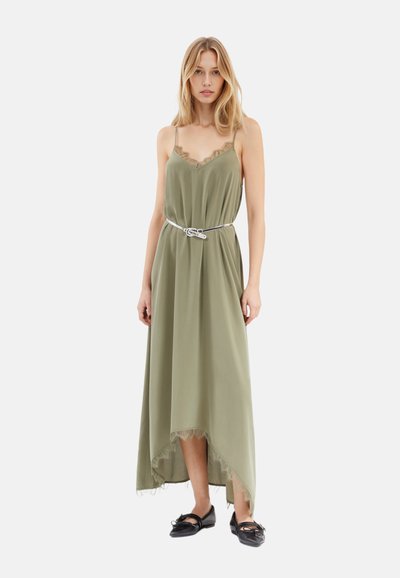 Robe vert olive avec des finitions en dentelle et des bretelles spaghetti réglables, dotée d'un ourlet asymétrique et d'une ceinture en argent à la taille. Chaussures noires.