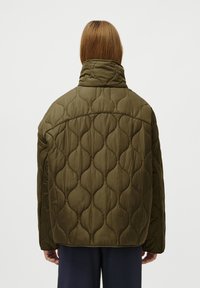 Casaco acolchoado verde-oliva com colarinho alto e textura volumosa, apresentando um padrão de onda e um corte solto e oversized.