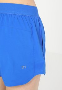 Blå sportshorts med ett elastiskt midjeband, sidoficka och en silverfärgad "D1"-logotyp på nedre vänstra benet. Slät, lättviktig material.