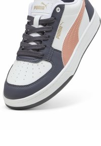 Puma-Sneaker mit einer weißen Lederzehe, grauen Einsätzen und einem rosafarbenen Akzent. Verfügt über eine runde Schnürung und eine perforierte Zehenpartie für Atmungsaktivität.