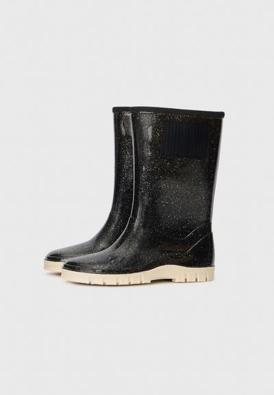 Bottes en caoutchouc noires brillantes, montantes jusqu'aux genoux, avec des éclats blancs et des semelles épaisses beiges, présentées côte à côte sur un fond uni.