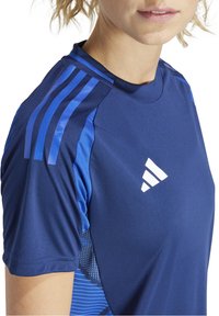 Maglietta sportiva navy con accenti blu, realizzata in tessuto traspirante, con scollatura rotonda e design a tre strisce sulle spalle. Presenta un logo bianco.