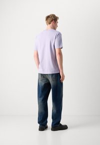 Lavendel bomull t-skjorte med korte ermer, kombinert med mørkeblå, lett slitte denimjeans og svarte, robuste sko.