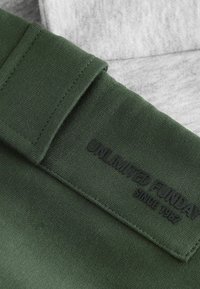 Green fabric with a smooth texture, featuring a folded cuff and an embossed brand label "UNLIMITED FUNDAY SINCE 1982" in black.