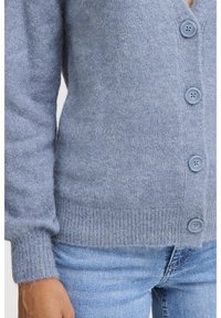 Ljusblå cardigan i mjukt, strukturerat material; har djup V-ringning, ribbad nederkant och sex matchande knappar fram.