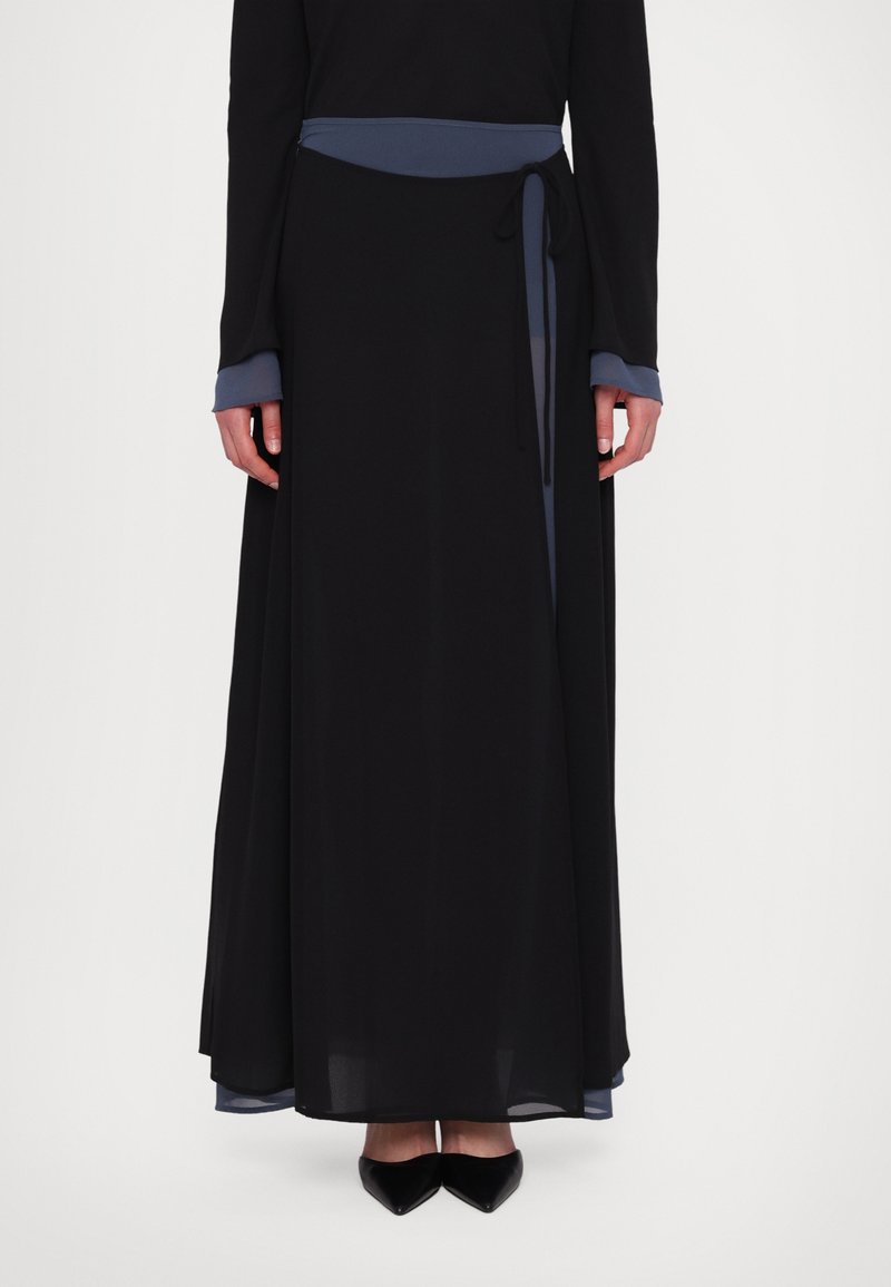 Lang sort kjole med blåt taljebånd og manchetter, der har en flydende silhuet og en gennemsigtig nederste kant. Stoffet virker let.