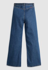 Jean en denim bleu à jambes larges vu de dos avec détail tressé à la taille et une petite étiquette rouge de la marque sur la poche droite.