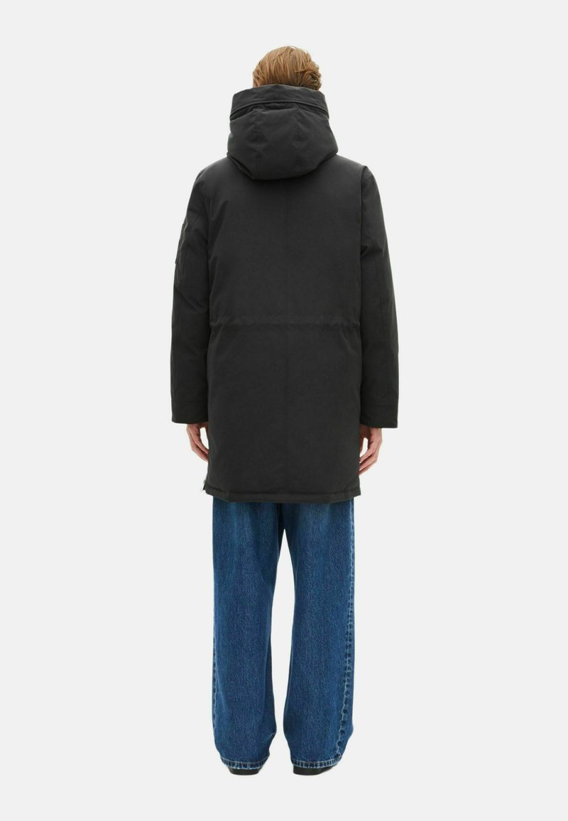 Black long coat with a hood, featuring a simple design and straight cut. Paired with loose, wide-leg blue jeans. Smooth texture.