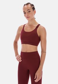 Bordový sportovní podprsenka s bezešvým designem, širokými ramínky a strukturovaným spodním pásem. V páru s vysokými bordovými legínami.