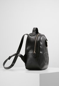 Sac à dos en cuir noir avec une forme arrondie, une finition texturée, une fermeture éclair dorée et un logo embossé à l'avant. Sangle réglable incluse.