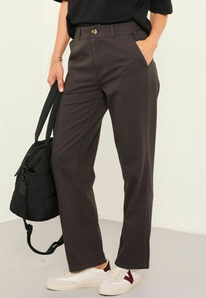 Dunkelbraune weite Hosen verfügen über einen Knopfverschluss und Seitentaschen. Getragen mit einem schwarzen Oberteil und weißen Sneakers mit burgunderfarbenen Akzenten.